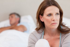 Sad woman on bed with her husband in the background
