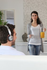 Woman carrying glass of juice to man wearing headphones